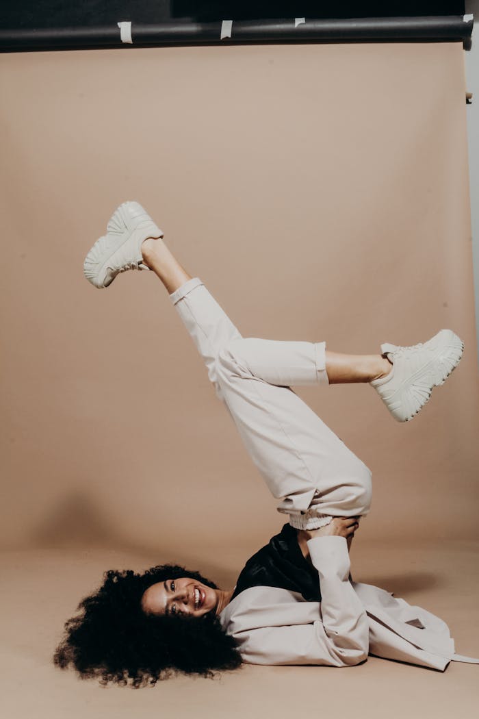 Young woman with afro hair striking a playful pose in a stylish studio fashion shoot. Light tones.